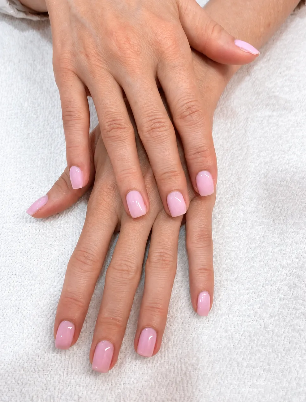 Two hands with soft pink Dazzle Dry lacquer resting on a white salon towel