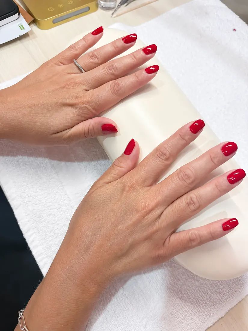 Two hands with glossy red Dazzle Dry lacquer resting at the manicure station