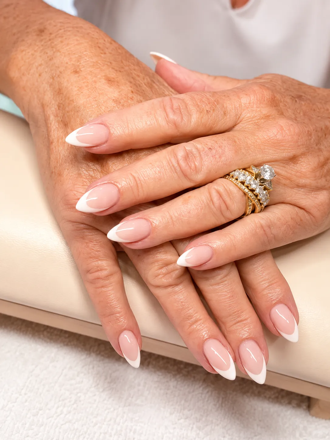 Hands resting on a cream cushion with almond-shaped polygel nails in a classic French finish