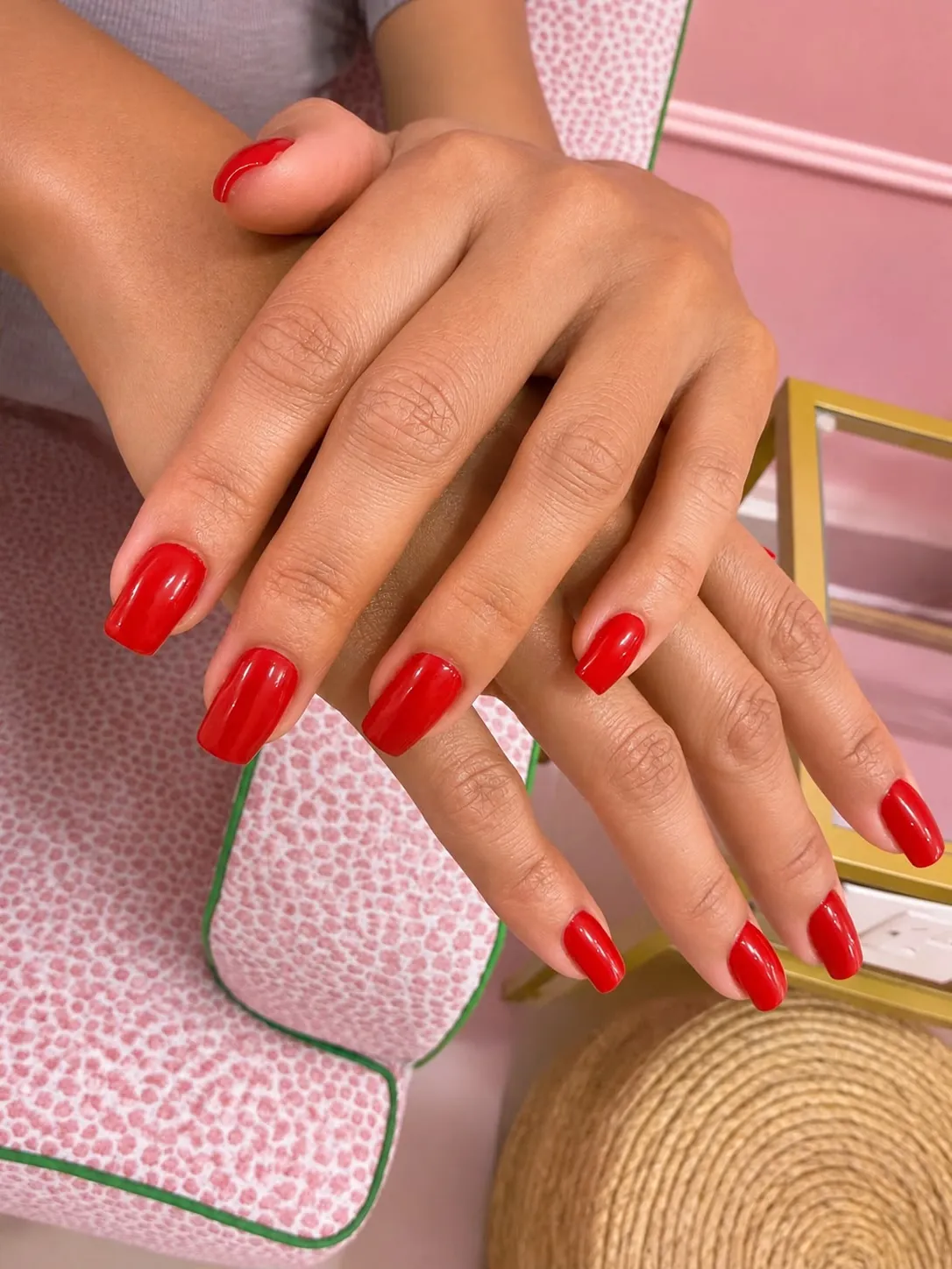 Close-up of hands with a glossy red Russian manicure, resting on a pink armchair at Palm Nail Lounge