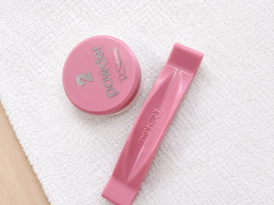 The P.Shine finishing powder and its pink buffer on a white towel