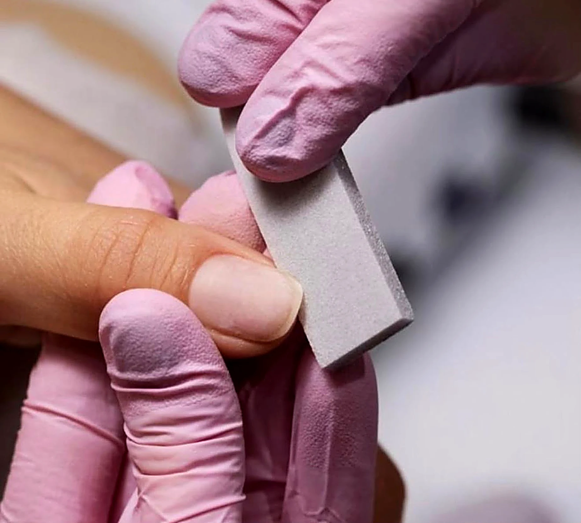 Technician gently buffing a natural nail with a soft block